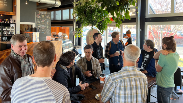 A group of 9 people chatting around a table in a coffee shop